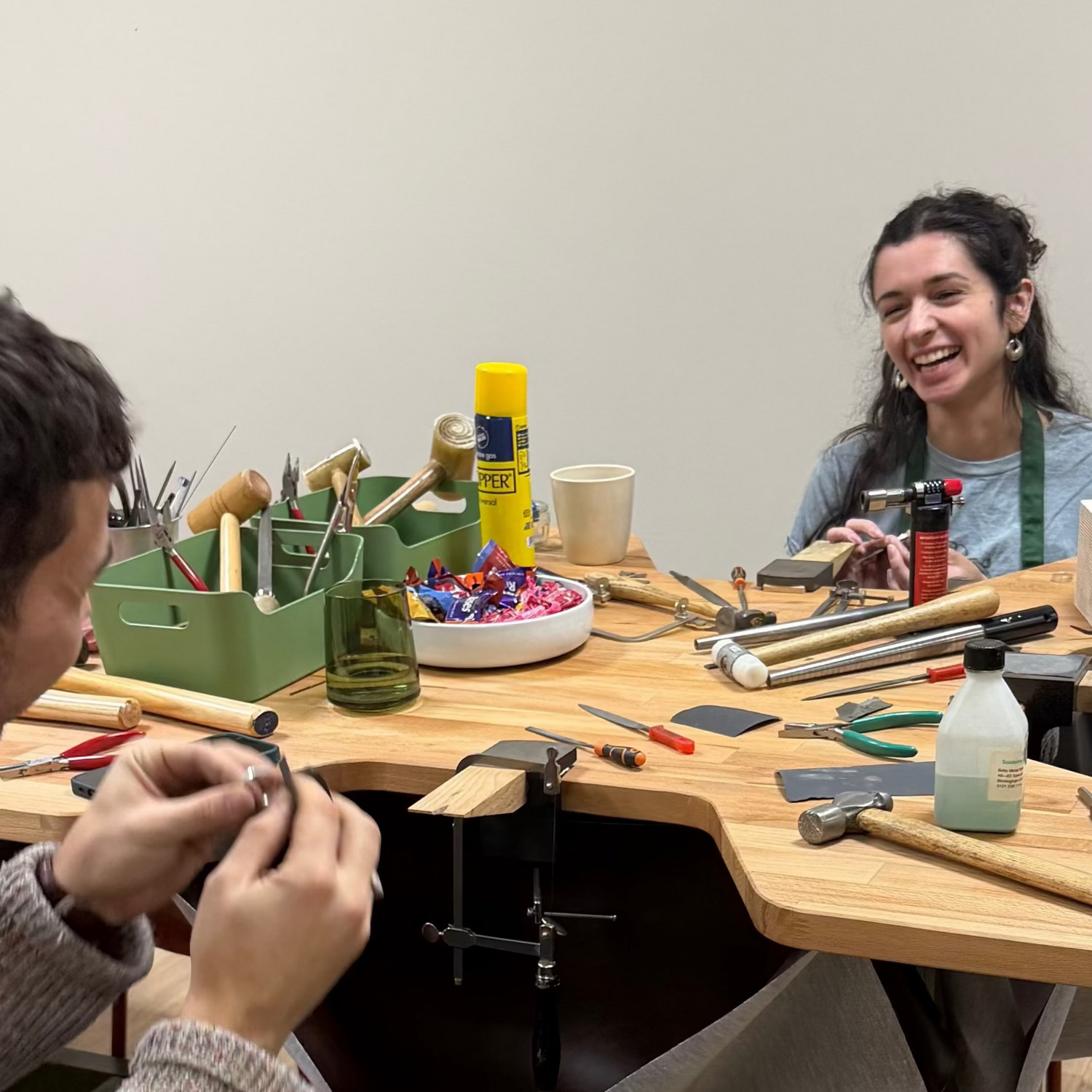 Two people sitting at a table with various tools and items, smiling and engaged in an activity.