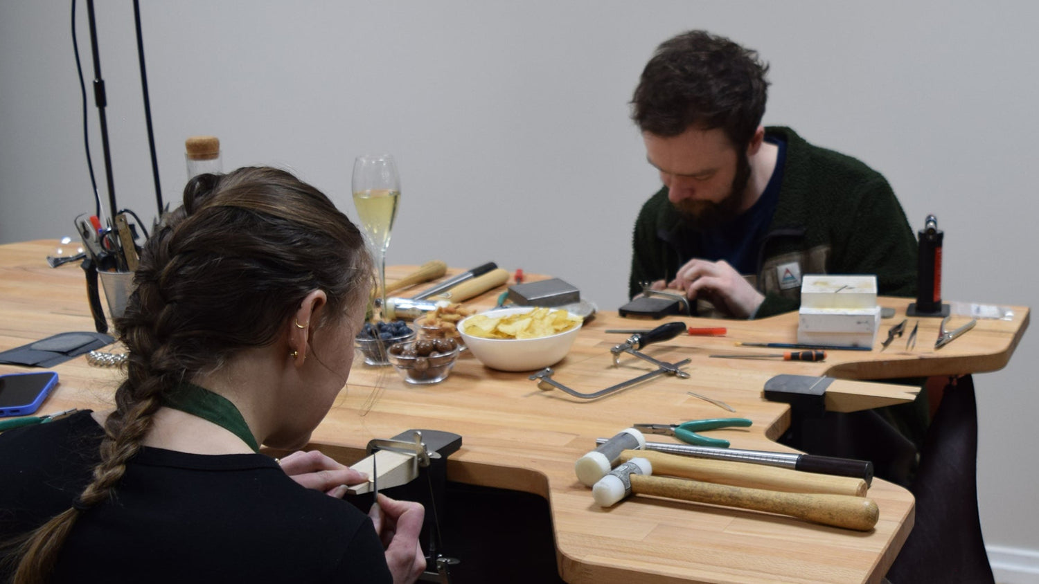 Two people working at a table with tools and snacks in a workshop setting.